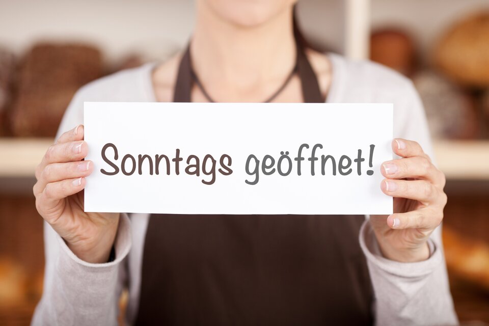 Frau hält Schild mit Sonntags geöffnet hoch Frau hält Schild mit Sonntags geöffnet hoch