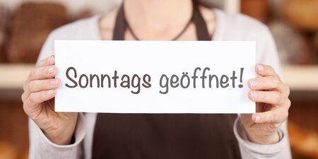 Frau hält Schild mit Sonntags geöffnet hoch Frau hält Schild mit Sonntags geöffnet hoch