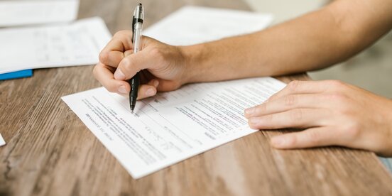 Eine Person füllt mit einem Kugelschreiber ein Formular aus – Symbolbild für Antragsverfahren im Rahmen des Gesetzes für einen inklusiven Arbeitsmarkt.