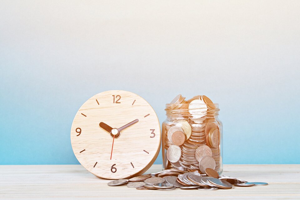 Ein Glas mit Münzen neben einer Holz-Uhr auf einem Tisch – das Bild steht symbolisch für die Betriebsratsvergütung und die Verbindung von Zeitaufwand und finanzieller Bewertung.