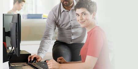 Ein Mann unterstützt eine Frau am Arbeitsplatz am Computer – Symbolbild für die Assistenz der Schwerbehindertenvertretung im Büroalltag. Ein Mann unterstützt eine Frau am Arbeitsplatz am Computer – Symbolbild für die Assistenz der Schwerbehindertenvertretung im Büroalltag.