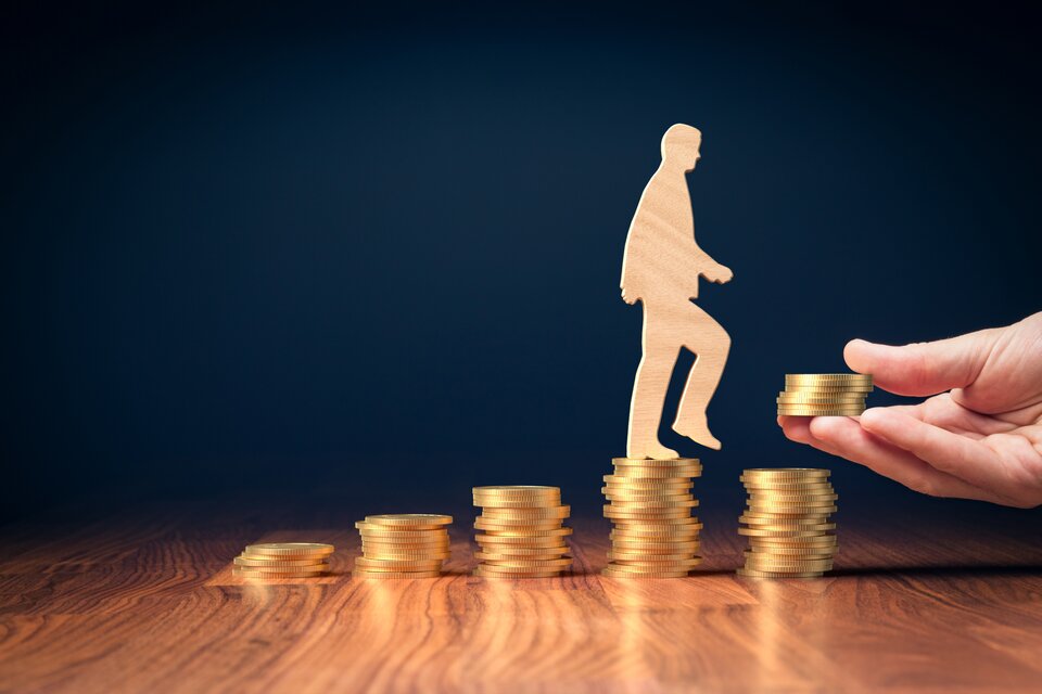 Holzfigur eines Menschen steigt eine Treppe aus Münzstapeln empor – Symbolbild für finanzielle Hilfen des Integrationsamts zur Arbeitsplatzsicherung von Menschen mit Behinderung. Holzfigur eines Menschen steigt eine Treppe aus Münzstapeln empor – Symbolbild für finanzielle Hilfen des Integrationsamts zur Arbeitsplatzsicherung von Menschen mit Behinderung.
