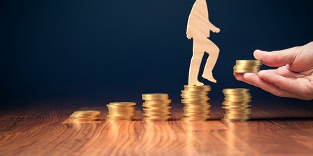 Holzfigur eines Menschen steigt eine Treppe aus Münzstapeln empor – Symbolbild für finanzielle Hilfen des Integrationsamts zur Arbeitsplatzsicherung von Menschen mit Behinderung. Holzfigur eines Menschen steigt eine Treppe aus Münzstapeln empor – Symbolbild für finanzielle Hilfen des Integrationsamts zur Arbeitsplatzsicherung von Menschen mit Behinderung.