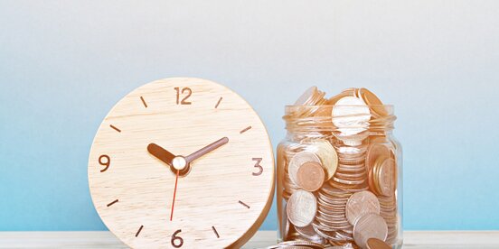 Eine Uhr und ein Glas voller Münzen symbolisieren die enge Verbindung von Zeit und Geld – zentrale Themen in der Diskussion über faire Bezahlung von Menschen mit Behinderung.