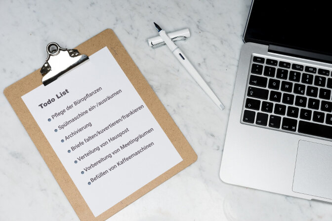 Clipboard mit einer To-do-Liste typischer Bürotätigkeiten neben Laptop und Stift – Symbolbild für Aufgaben beim Job Carving zur Schaffung inklusiver Arbeitsplätze. Clipboard mit einer To-do-Liste typischer Bürotätigkeiten neben Laptop und Stift – Symbolbild für Aufgaben beim Job Carving zur Schaffung inklusiver Arbeitsplätze.