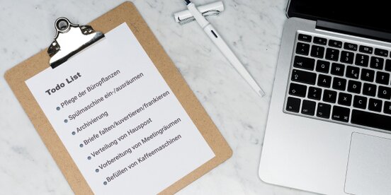 Clipboard mit einer To-do-Liste typischer Bürotätigkeiten neben Laptop und Stift – Symbolbild für Aufgaben beim Job Carving zur Schaffung inklusiver Arbeitsplätze.