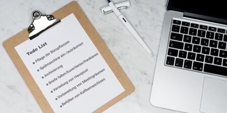 Clipboard mit einer To-do-Liste typischer Bürotätigkeiten neben Laptop und Stift – Symbolbild für Aufgaben beim Job Carving zur Schaffung inklusiver Arbeitsplätze. Clipboard mit einer To-do-Liste typischer Bürotätigkeiten neben Laptop und Stift – Symbolbild für Aufgaben beim Job Carving zur Schaffung inklusiver Arbeitsplätze.