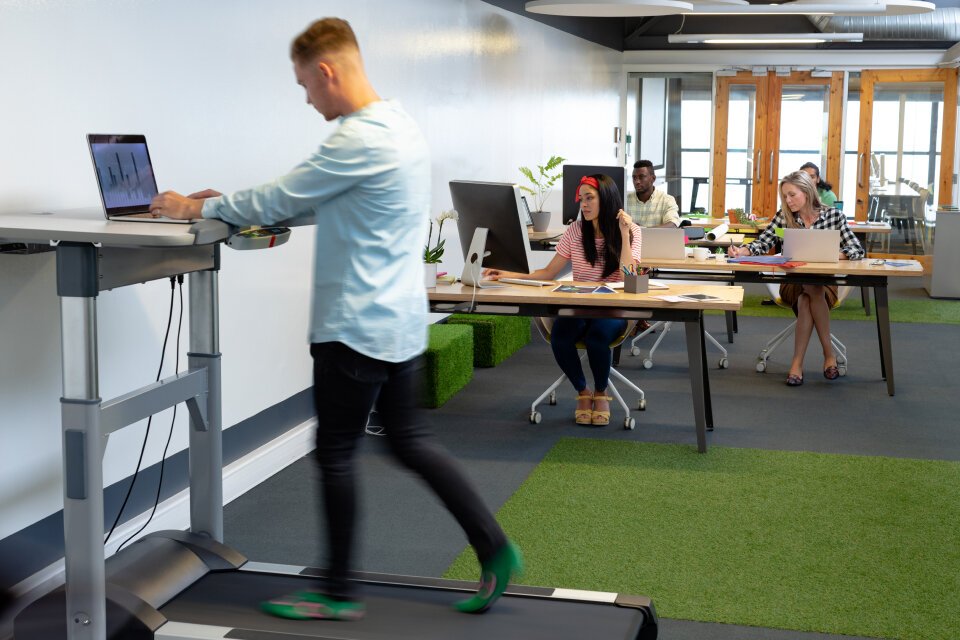 Ein Mitarbeiter arbeitet im Stehen an einem höhenverstellbaren Schreibtisch mit integriertem Laufband – modernes Büro als Beispiel für ergonomische Arbeitsplatzgestaltung und gelebten Arbeitsschutz. Ein Mitarbeiter arbeitet im Stehen an einem höhenverstellbaren Schreibtisch mit integriertem Laufband – modernes Büro als Beispiel für ergonomische Arbeitsplatzgestaltung und gelebten Arbeitsschutz.