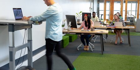Ein Mitarbeiter arbeitet im Stehen an einem höhenverstellbaren Schreibtisch mit integriertem Laufband – modernes Büro als Beispiel für ergonomische Arbeitsplatzgestaltung und gelebten Arbeitsschutz. Ein Mitarbeiter arbeitet im Stehen an einem höhenverstellbaren Schreibtisch mit integriertem Laufband – modernes Büro als Beispiel für ergonomische Arbeitsplatzgestaltung und gelebten Arbeitsschutz.