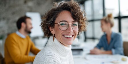 Frau mit weißem Pullover und Brille sitzt im Meeting mit zwei Kollegen