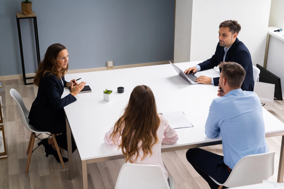 Vier Personen sitzen an einem Besprechungstisch in einem modernen Büro und führen ein Gespräch. Vier Personen sitzen an einem Besprechungstisch in einem modernen Büro und führen ein Gespräch.