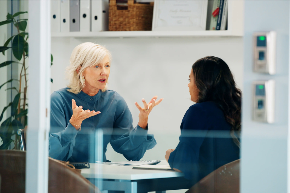 Zwei Personen sitzen an einem Besprechungstisch in einem Büro und führen ein Gespräch. Zwei Personen sitzen an einem Besprechungstisch in einem Büro und führen ein Gespräch.