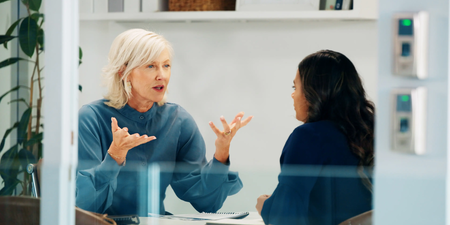 Zwei Personen sitzen an einem Besprechungstisch in einem Büro und führen ein Gespräch.