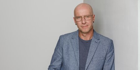 Ein Mann mit Anzug steht vor einer grauen Wand Ein Mann mit Anzug steht vor einer grauen Wand