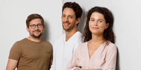 Drei Kollegen stehen vor einer grauen Wand Drei Kollegen stehen vor einer grauen Wand