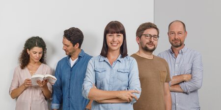Fünf Kollegen stehen vor einer grauen Wand