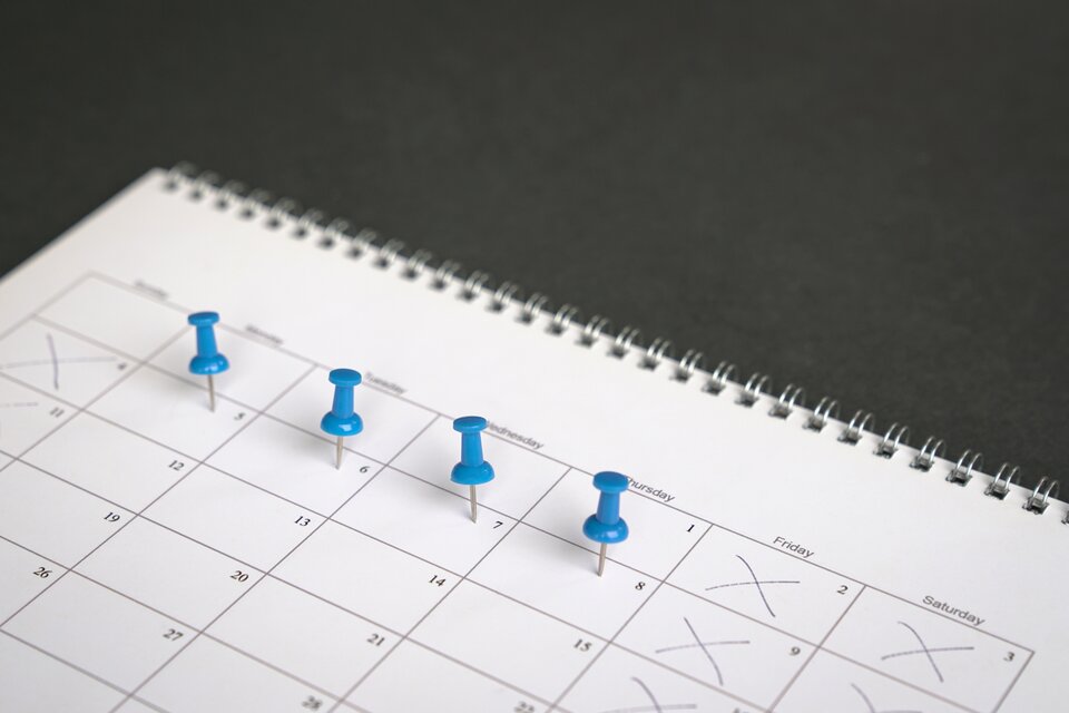 Auf einen Kalender sind Tage mit Stecknadeln markiert Auf einen Kalender sind Tage mit Stecknadeln markiert