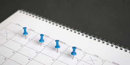 Auf einen Kalender sind Tage mit Stecknadeln markiert Auf einen Kalender sind Tage mit Stecknadeln markiert
