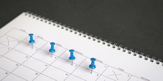 Auf einen Kalender sind Tage mit Stecknadeln markiert Auf einen Kalender sind Tage mit Stecknadeln markiert