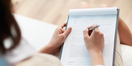 Eine Frau schreibt auf einen Blatt den Teilhabeverfahrensbericht Eine Frau schreibt auf einen Blatt den Teilhabeverfahrensbericht