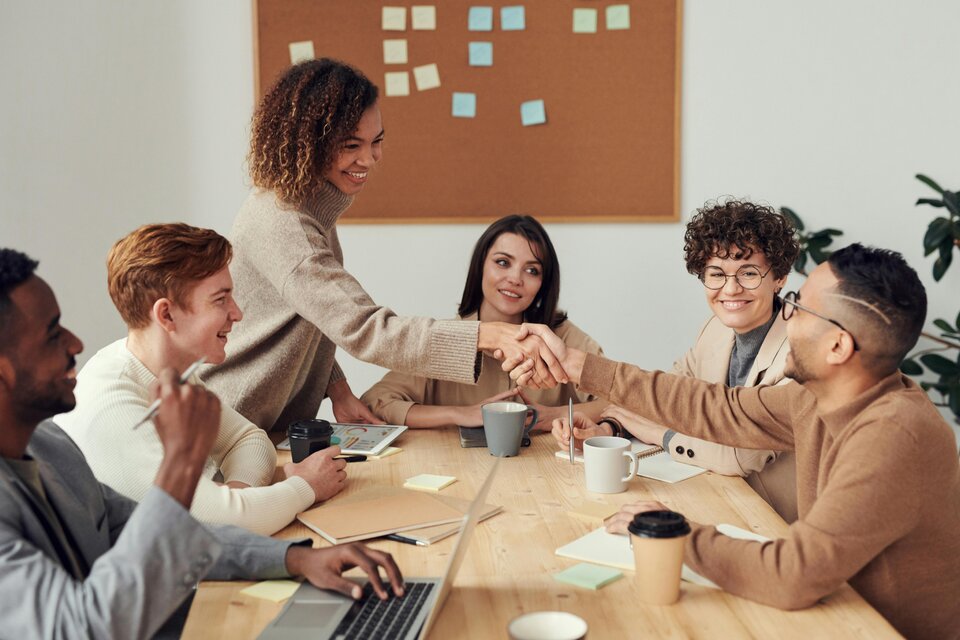 Ein fröhliches Team in einem Meetingraum, zwei Personen geben sich zur Begrüßung die Hand – das Bild symbolisiert gelungene Zusammenarbeit und erfolgreiche Klausurtagung im Betriebsrat. Ein fröhliches Team in einem Meetingraum, zwei Personen geben sich zur Begrüßung die Hand – das Bild symbolisiert gelungene Zusammenarbeit und erfolgreiche Klausurtagung im Betriebsrat.