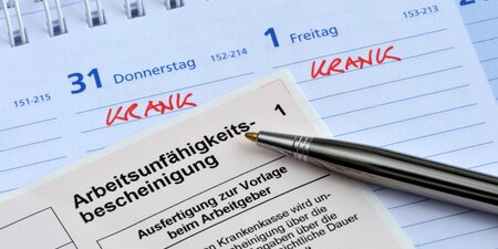 Arbeitsunfähigkeitsbescheinigung mit Kugelschreiber auf einem Kalender, in dem mehrere Tage als „krank“ markiert sind – Symbolbild für Entgeltfortzahlung im Krankheitsfall. Arbeitsunfähigkeitsbescheinigung mit Kugelschreiber auf einem Kalender, in dem mehrere Tage als „krank“ markiert sind – Symbolbild für Entgeltfortzahlung im Krankheitsfall.