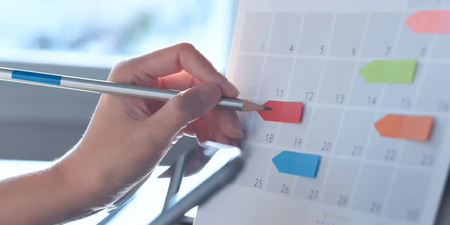 Hand markiert ein Datum auf einem Kalender mit bunten Markierungen – Symbol für den Wahlkalender der Betriebsratswahl.