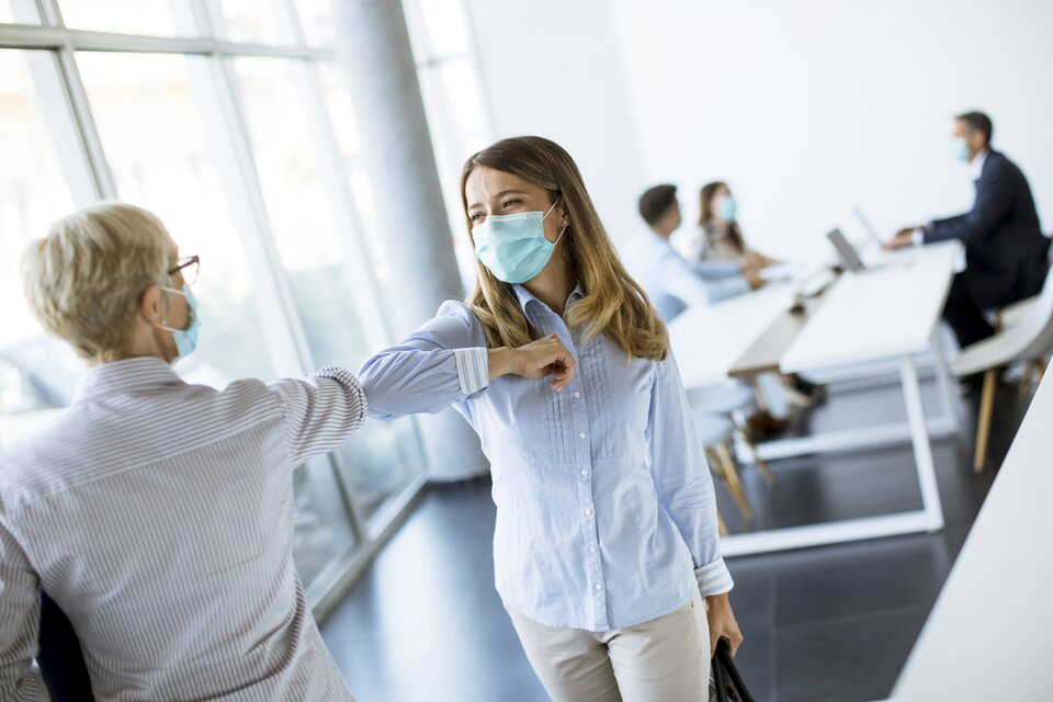 Zwei Frauen tragen eine Corona Maske und geben sich einen Ellbogen-Check