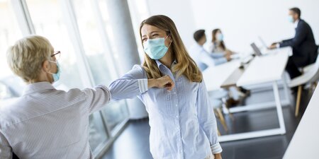 Zwei Frauen tragen eine Corona Maske und geben sich einen Ellbogen-Check Zwei Frauen tragen eine Corona Maske und geben sich einen Ellbogen-Check