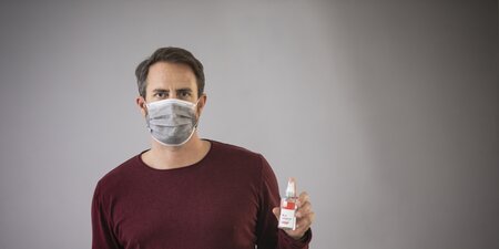 Ein Mann trägt eine Corona Maske und ein Desinfektionsspray in der Hand Ein Mann trägt eine Corona Maske und ein Desinfektionsspray in der Hand