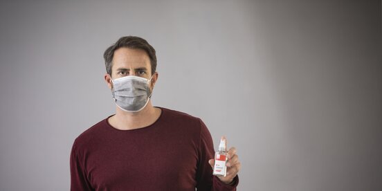 Ein Mann trägt eine Corona Maske und hat ein Desinfektionsspray in der Hand Ein Mann trägt eine Corona Maske und hat ein Desinfektionsspray in der Hand