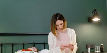 Kind liegt Krank im Bett und Mutter passt auf