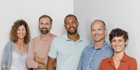 Fünf Kollegen stehen vor einer grauen Wand Fünf Kollegen stehen vor einer grauen Wand
