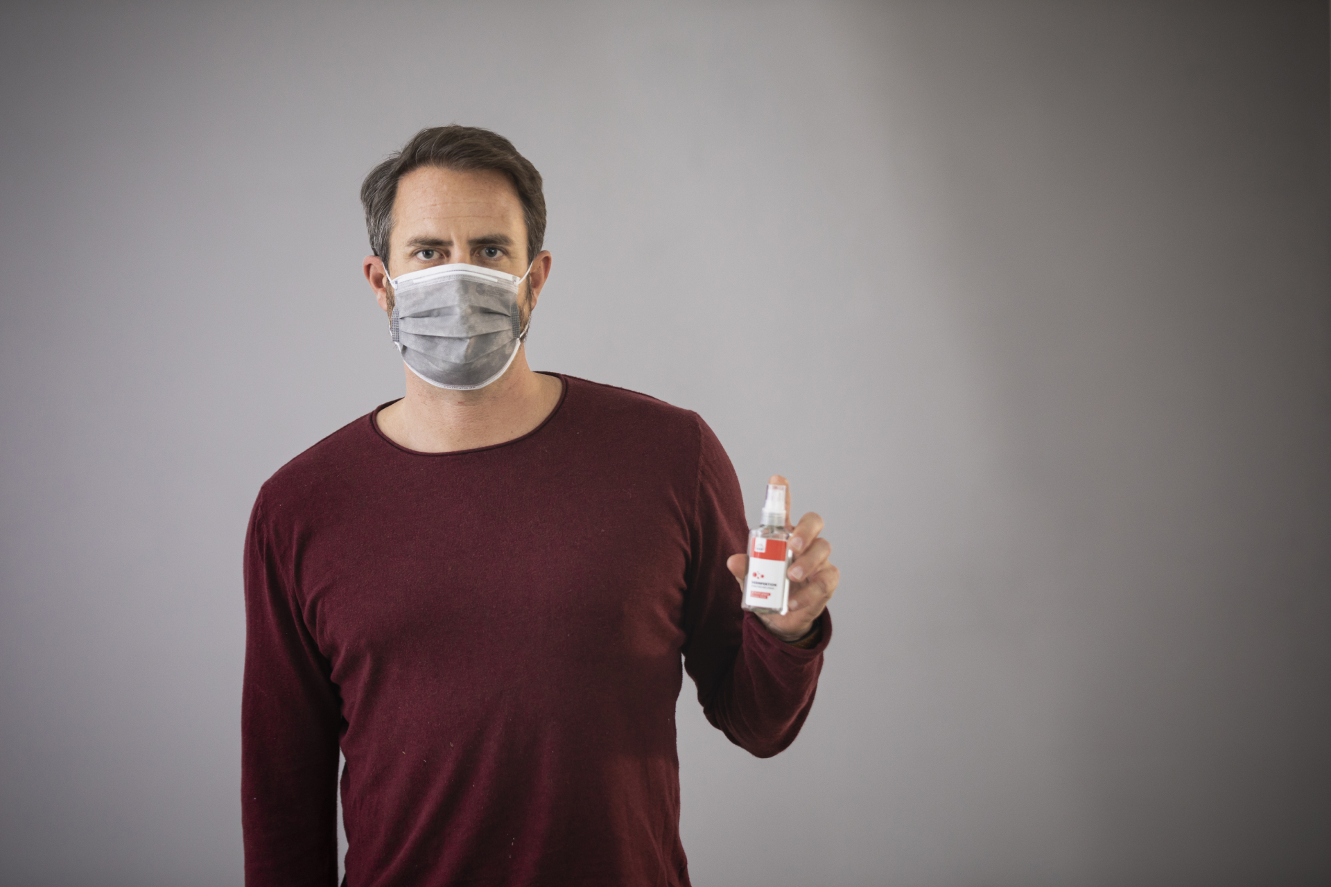 Ein Mann trägt eine Corona Maske und ein Desinfektionsspray in der Hand