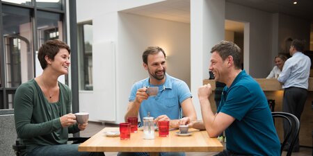 Drei Kollegen unterhalten sich und trinken einen Kaffee Drei Kollegen unterhalten sich und trinken einen Kaffee