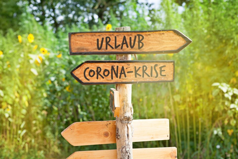 Ein Schild mit Urlaub und in die andere Richtung geht ein Schild mit Corona-Krise Ein Schild mit Urlaub und in die andere Richtung geht ein Schild mit Corona-Krise