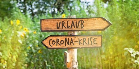 Ein Schild mit Urlaub und in die andere Richtung geht ein Schild mit Corona-Krise Ein Schild mit Urlaub und in die andere Richtung geht ein Schild mit Corona-Krise