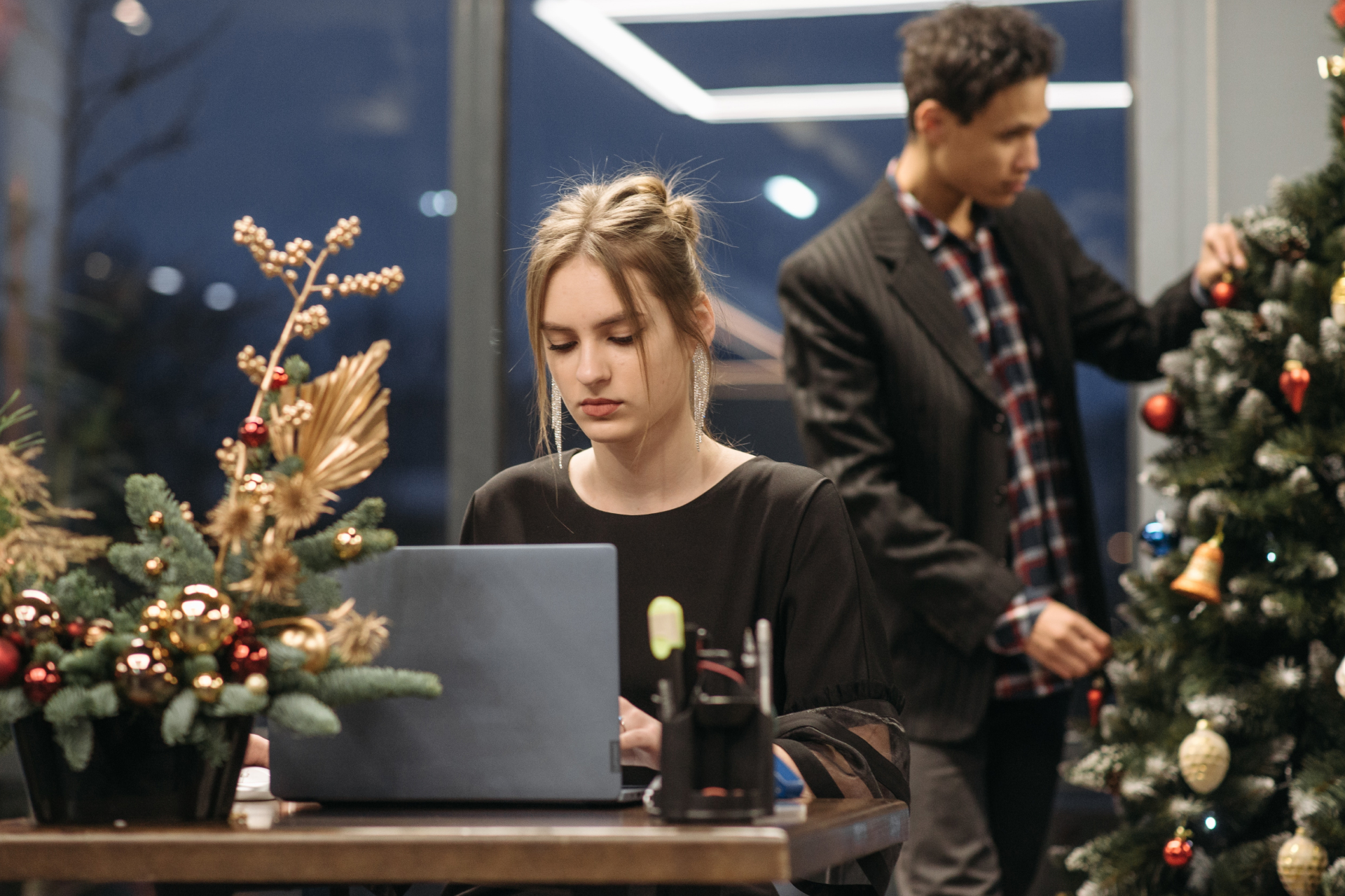 Ein Mann schmückt den Weihnachtsbaum und eine Frau arbeitet am Laptop