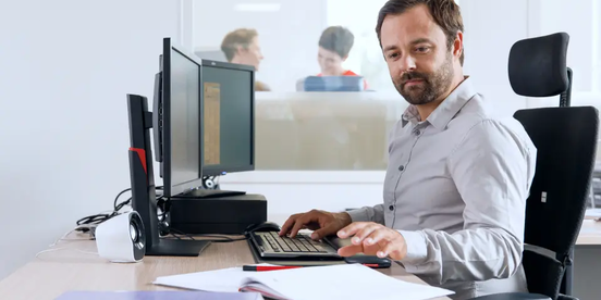 Mann arbeitet am Computer mit Dokumenten auf dem Schreibtisch – Symbol für die Berechnung der Betriebsratsgröße.
