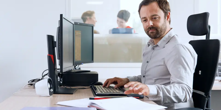 Mann arbeitet am Computer mit Dokumenten auf dem Schreibtisch – Symbol für die Berechnung der Betriebsratsgröße.